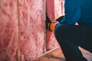 Handwerker befestigt Bauteil an einer mit rosa Dämmstoff gefüllten Wand